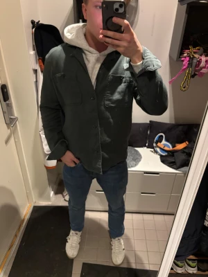 Mörkgrön overshirt från Dressmann - Snygg mörkgrön overshirt från Dressmann i bomull. Skjortan har två bröstfickor med knappar, klassisk krage och långa ärmar. Perfekt att bära öppen över en hoodie eller t-shirt 