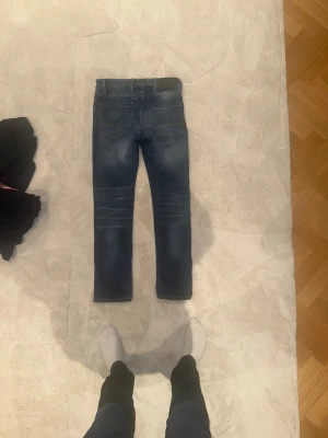 Jack and Jones , storlek 28/30 - Snygga blå Jack and Jones jeans med klassisk femficksdesign och slitningar på låren. Jeansen har smal passform och är tillverkade i stretchigt denim för extra komfort. Perfekt för dig som gillar en modern och stilren look.