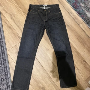 mörkblå jeans straight fit -  jeans i mörkblå denim med raka ben och snygga kontrastsömmar. Modellen har fem fickor, knappgylf och läderpatch bak i midjan. Perfekta för dig som gillar tidlös och clean stil.