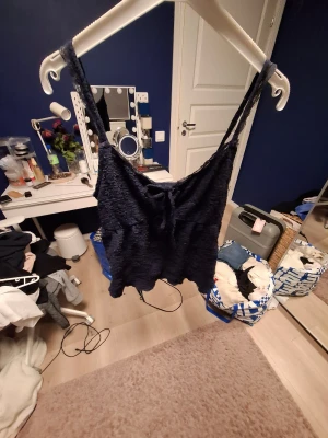 Mörkblå spetslinne från Gina Tricot - Supersöt mörkblå linnetopp från Gina Tricot i storlek XS. Toppen har tunna axelband och är dekorerad med spetsdetaljer längs kanterna. Materialet är mjukt och lätt, perfekt för varma dagar eller lager på lager. Snygg volangkant nedtill för extra stilpoäng.