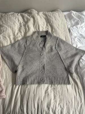 Grå bolero från Life Time - Grå bolero/kofta från Life Time med breda korta ärmar och stora knappar framtill. Stickad i mjukt material med ribbad krage och nederkant💓