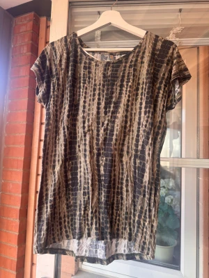 Leopardmönstrad topp - Säljer en topp med leopardmönster i svart och beige toner. Modellen är loose fit med rund hals och korta ärmar. Materialet känns mjukt och lätt. Storlek XS