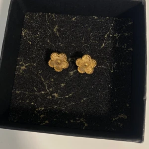 Örhängen i rostfritt stål  - Supersöta örhängen i form av små blommor i guldig färg. De har fina detaljerade blad och en liten kula i mitten som ger dem en elegant och trendig look. Perfekta för att lyfta vilken outfit som helst. Ask ingår ej