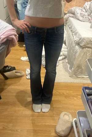 Blå bootcut low waist jeans  - Snygga blå bootcut low waisted jeans från Please med låg midja och fem knappar framtill. Jeansen har klassisk femficksdesign, coolt sliten tvätt och ett litet hjärtdetalj på bakfickan. Tillverkade i mjukt jeansmaterial med skön passform. 