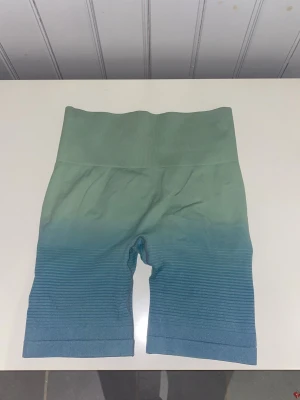 Grön-blå seamless biker shorts - Säljer av alla mina träningsshorts nu då jag behöver större storlek. Så om du är sugen på flera kan jag fixa paketpris o skicka dom i samma. Men detta är ett par  seamless biker shorts med hög midja i en grön till blå ombre. De har ribbade detaljer på benen. Går att ha långa men även vika upp dom utan att det blir obekvämt. Dom är i storlek S