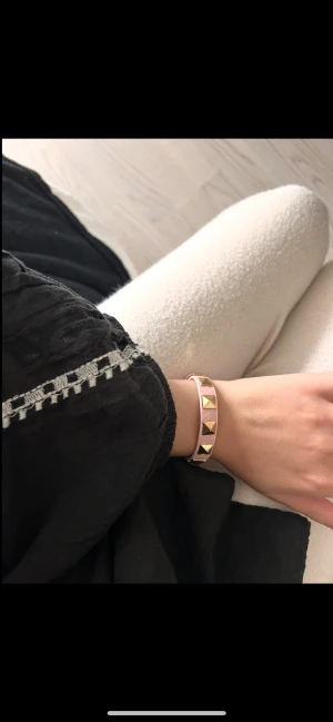 Valentino armband med nitar i rosa skinn - Säljer ett snyggt Valentino-armband i ljusrosa skinn med guldiga pyramidformade nitar. Armbandet har en stilren och edgy look som verkligen sticker ut. Perfekt accessoar för dig som vill addera lite lyx och attityd till din outfit.