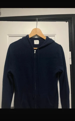 Mörkblå Kashmir hoodie John Henric - Mjuk och lyxig mörkblå hoodie från John Henric i 100% cashmere. Tröjan har huva, dragkedja framtill och två fickor. Perfekt för dig som vill ha en stilren och bekväm look med premiumkänsla.  Perfekt för hösten/vintern