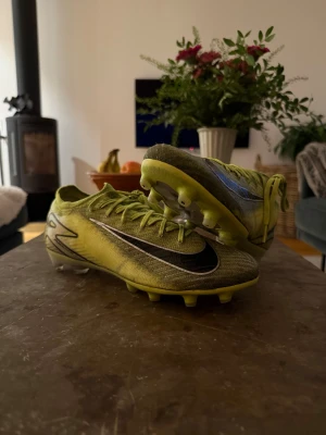 Nike Mercurial fotbollsskor grön - Säljer ett par Nike Mercurial Vapor elit fotbollsskor ag/konstgräs i en grön-gul färg med svarta och silvriga detaljer. Skorna har snörning, platt sula med dobbar och en sportig, aerodynamisk design. Perfekta för dig som vill sticka ut på planen och få grymt grepp på planen. PRIS KAN DISKUTERAS! 