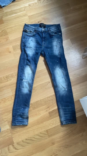 Supply & Demand skinny jeans blå XS - Blå skinny jeans från Supply & Demand i storlek XS med coola slitningar och blekta detaljer på benen. Jeansen har klassisk femficksdesign, smal passform och små vita färgstänk som ger en edgy vibe. Perfekt för dig som gillar streetstyle.