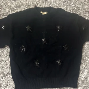 Svart stickad tröja med paljettstjärnor - Svart stickad tröja från Gina Tricot med flera glittriga paljettstjärnor på framsidan. 