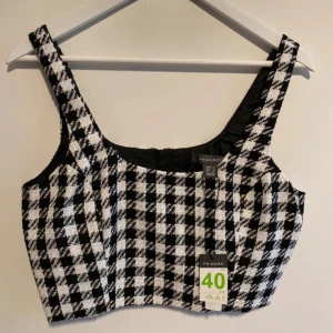 Svartvit rutig korsett crop top från Primark - New with label. Säljer en snygg korsett-topp från Primark i storlek 40. Toppen har ett svartvitt rutigt mönster och är croppad med breda axelband. Materialet är grovt vävt och ger en cool textur. Perfekt för dig som gillar statement-plagg och vill sticka ut.