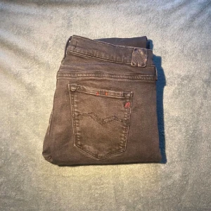Svarta Replay jeans 32/30 - Svarta jeans från Replay  med klassisk femficksdesign och diskreta röda detaljer på bakfickan. Jeansen har normal midja och är tillverkade i stretchigt denim för en tajt och bekväm passform. Perfekta för dig som gillar en stilren look.