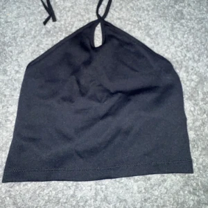 Svart ribbad halterneck linnetopp - Säljer en svart halterneck linnetopp med ribbad struktur och knyt i nacken. Toppen har en liten öppning framtill vid halsen och är croppad i modellen. Perfekt för dig som gillar minimalistisk stil och vill ha en enkel men snygg topp till sommaren.