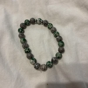 Grått och grönt pärlarmband - Snyggt armband med runda pärlor i grått och grönt, vissa med marmorerat mönster. Elastiskt band gör det enkelt att ta på och av. Perfekt accessoar för att ge din outfit en cool och unik touch.