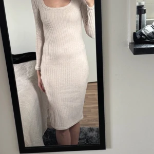 Beige ribbad långärmad klänning - Säljer en beige ribbad klänning med lång ärm och rundad halsringning. Klänningen är figurnära och har en snygg slits på sidan som ger extra edge. Materialet är stickat och mjukt, perfekt för dig som gillar stilren och enkel design.