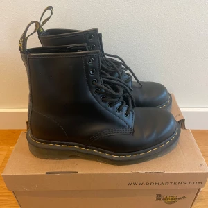 Dr. Martens - Svarta Boots stl 40 - Klassiska svarta Dr. Martens boots i skinn med rund tå/stålhätta och snörning. Dessa är i nyskick, inga repor eller liknande. Använda endast en gång. Nypris 1899 kr.