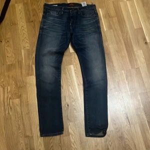 Mörkblå jeans från Jack & Jones - Snygga mörkblå jeans från Jack & Jones med klassisk femficksdesign och diskret slitning på låren. Jeansen har raka ben och normal passform, tillverkade i bomull med en skön jeanskänsla. Perfekta för en avslappnad och stilren look.