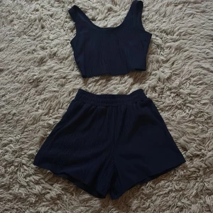 Mörkblå croppad linnetopp och shorts - Säljer en stilren mörkblå croppad linnetopp och shorts med breda axelband. Toppen är gjord i ett mjukt, lätt skrynkligt material som känns skönt mot huden. Perfekt för dig som gillar enkel och clean look. Matcha med shorts eller jeans för en chill vibe.