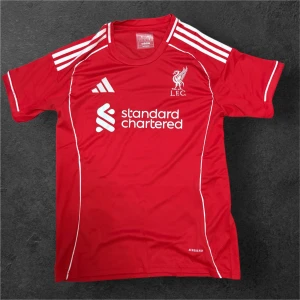 Liverpool röd fotbollströja Adidas - Snygg röd Liverpool fotbollströja från Adidas med vita detaljer och tryck. Tröjan har korta ärmar, klassiska Adidas-ränder på axlarna och klubbens logga på bröstet. Materialet är lätt och andas, perfekt för träning eller match.