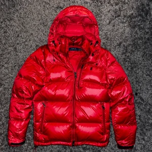 Ralph Lauren jacka - Säljer en fet röd pufferjacka från Polo Ralph Lauren i storlek XS. Jackan har huva med snörning, flera fickor med dragkedja och en glansig finish. Perfekt för kalla dagar och har en riktigt schysst streetstil. Klassisk Polo-logga på bröstet, samt en Grisch stil med en cool vinter jacka🥶💸🤑