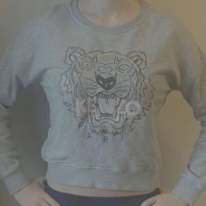 Grå collegetröja kenzo - Säljer en grå sweatshirt från Kenzo. Modellen är lite kortare och passar snyggt med lågmidjade jeans. Tröjan har rund hals, ribbade muddar och är i mjuk bomullsblandning. Lite coolare och unikare tröja.xs-s