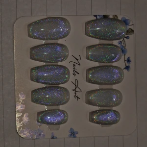 Holografiska lösnaglar Nails Art. Lim, sticki pads & rengöring ingår med naglarna. nagel storlek: M - Säljer ett set med 12 holografiska lösnaglar från Nails Art. Naglarna har en skimrande silverbas med regnbågsglitter och oval form. Perfekt för dig som vill ha extra glans och wow-effekt på naglarna. och de kommer i olika storlekar för att passa alla fingrar.