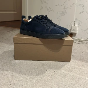 Mörkblå mocka sneakers från Louboutin - Säljer ett par exklusiva mörkblå sneakers från Christian Louboutin i lyxig mocka. Skorna har rund tå, platt sula och snygg snörning. Diskret broderad logga baktill och klassisk design. Kommer med originalkartong och dustbag.