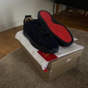 Mörkblå sneakers från Christian Louboutin - Snygga mörkblå sneakers från Christian Louboutin i mocka med klassisk röd sula och diskret logga. Skorna har rund tå, snörning och platt sula. Perfekta för dig som vill ha en lyxig och stilren look med en ikonisk touch. HELT OANVÄNDA!!!