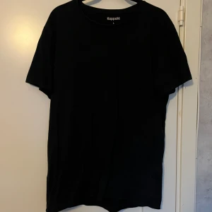 Svart t-shirt från Kappahl, storlek L - En enkel svart t-shirt från Kappahl i storlek L. Modellen har rund hals och korta ärmar, tillverkad i mjuk bomull som känns skön mot huden. Den har ett acceptabelt skick men den har blivit lite urtvättad annars inget fel på den. Hör av er om ni har frågor!