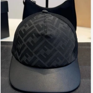 Svart keps från Fendi med logomönster - Snygg svart keps från Fendi med ikoniskt logomönster över hela framsidan. Kepsen har böjd skärm i ett slätt material och mesh på sidorna för extra ventilation. Perfekt accessoar för en trendig streetstyle-look.