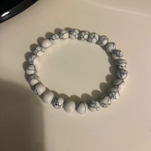 Vitt pärlarmband med marmormönster - Snyggt armband med vita runda pärlor som har ett coolt marmormönster i grått. Perfekt för dig som gillar stilrena accessoarer med en twist. Elastiskt band gör det enkelt att ta på och av. Passar till många olika looks!