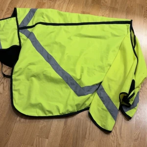 Reflex täcke gul och orange + benskydd  - Säljer tre reflex täcken + benskydd , två i neon-gul och en i neon-orange med breda gråa reflexband. Täckena har svart foder och kant, och är designade för att ge extra synlighet vid uteritt. Perfekt för dig som vill synas i trafiken eller på mörka ridvägar.