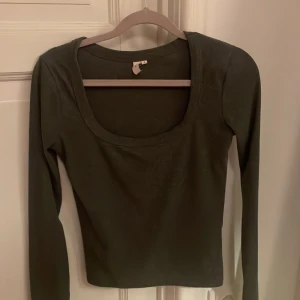 Mörkgrön långärmad topp med djup ringning - Snygg mörkgrön långärmad topp från Nelly med djup rundad ringning. Modellen är slim och passar perfekt till jeans eller kjol. Materialet är mjukt och stretchigt, vilket gör den skön att bära hela dagen.