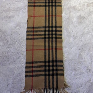 Beige rutig halsduk med fransar - Snygg beige halsduk med klassiskt rutigt mönster i svart och rött. Mjuk och varm, perfekt att slänga över axlarna när det är kallt ute. Fransar i ändarna ger en chill vibe. Passar dig som gillar tidlös stil och vill ha något som sticker ut. OBS INTE ORG1NAL