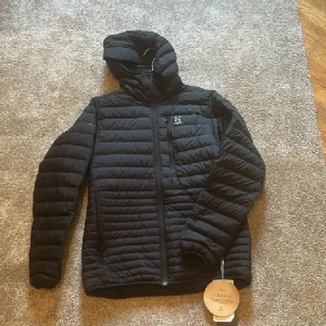 Svart dunjacka med huva från Haglöfs - Säljer en svart dunjacka från Haglöfs, modell Micro Nordic Down Hood. Jackan har huva, dragkedja framtill och quiltad design med horisontella sömmar. Perfekt för kalla dagar och har en stilren look med diskret logga på bröstet. Passar även S se sista bilden killen är S