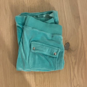 Turkosa mjukisbyxor Juicy Couture XXS - Säljer ett par turkosa mjukisbyxor från Juicy Couture i storlek XXS. Byxorna har bred resår med snörning i midjan, fickor med lock och silverfärgade knappar samt broderad Juicy-logga på ena fickan. Materialet är mjukt och skönt, skriv om ni har några funderingar💕