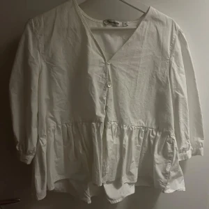 Vit blus med volang från Carin Wester - Säljer en söt vit blus från Carin Wester i storlek 34. Blusen har v-ringning, knappar framtill och volang nedtill som ger en flowy känsla. Långärmad och tillverkad i mjuk bomull. Perfekt för dig som gillar romantisk och enkel stil.