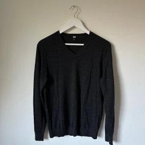 Mörkgrå v-ringad ulltröja från Uniqlo - Klassisk mörkgrå v-ringad tröja från Uniqlo i 100% ull. Den har lång ärm och en clean, stilren look som funkar till allt. Perfekt för lager-på-lager och enkel att matcha med både jeans och chinos. 4F5