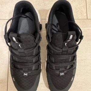 Nike Free svartvita sneakers - Svarta Nike Free sneakers med chunky vit sula och svart swoosh på sidan. Ovandelen är i mesh och syntet med snörning och låg profil. Skorna har rund tå och platt sula, perfekt för dig som gillar sportig och modern stil.