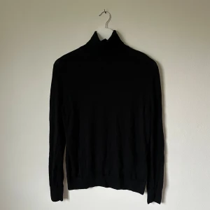 Svart polotröja i ull från Uniqlo - Svart polotröja från Uniqlo i storlek L, tillverkad i 100% ull. Tröjan har lång ärm och klassisk polokrage som ger en clean och stilren look. Perfekt att styla med jeans eller dressade byxor för en enkel vibe. 4D16