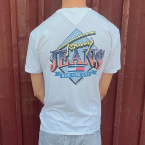 🕰️Billig Vintage tshia! Vit Tommy Jeans T-shirt - Vit Tommy Jeans T-shirt i storlek S (men passar M). Skön loose fit T-shirt med tryck i lätt bomull. Lite missfärgad vid halsen – därav priset. 🧼 Går eventuellt att bleka bort ✨Snygg till skolan chill-outfits 💸 Endast 159 kr – kap! 🚚 Frakten gratis🌟