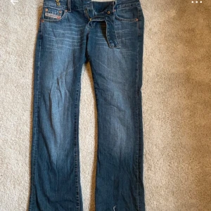 Blå bootcut jeans från Diesel - Säljer ett par snygga blå jeans från Diesel med bootcut passform. Klassisk femficksmodell med dragkedja och knapp i midjan. Jeansen har ljusa slitningar och detaljerade sömmar. Midjemåttet är 39cm innerbenslängden är 75cm Pris kan diskuteras 