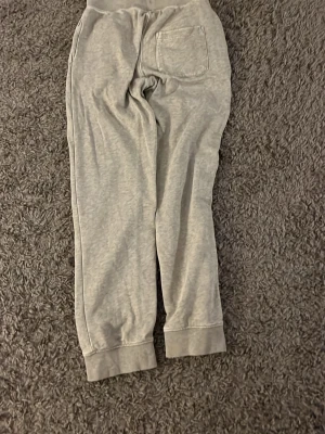 Gråa mjukisbyxor från Sail Racing - Mysiga grå mjukisbyxor från Sail Racing med snörning i midjan och en bakficka. Tillverkade i bomullsmaterial och har ribbade muddar vid bensluten. Perfekta för chill dagar eller bara för stil. Ncackdelen är att det finns väldigt små hål på baksidan men märks nästan inte då dem går att använda likadant.