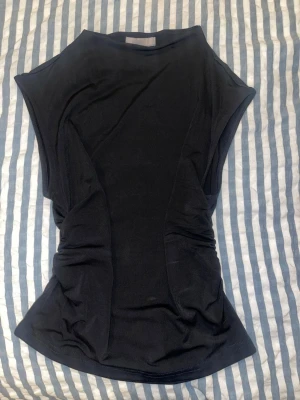Svart ärmlös topp från H&M - Snygg svart topp från H&M i stretchigt material. Modellen är ärmlös med markerade axlar och lätt rynkade sidor som ger en cool siluett. Perfekt att styla med jeans eller kjol för en trendig look. Använd fåtal gånger och fint skick💕