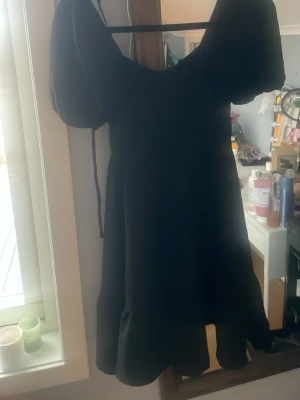 Svart kort puffärmad klänning Gina Tricot - Supersöt svart klänning från Gina Tricot med puffärmar och en lätt utställd kjol. Klänningen har en feminin siluett och är perfekt för dig som gillar trendiga detaljer. Tillverkad i ett mjukt tyg som känns bekvämt hela dagen.