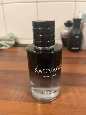 Dior Sauvage Eau de Parfum - Säljer en Dior Sauvage Eau de Parfum. Flaskan är cylinderformad i glas med en snygg svart till transparent färgskiftning och tydlig logga. Lock i svart plast med silverdetaljer. En ikonisk doft som känns lyxig och modern.