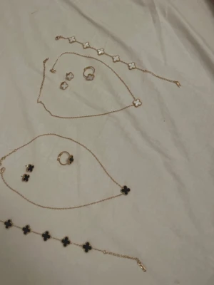 Guldarmband med svarta klöver - Snyggt armband i guldton med flera svarta klöverformade hängen. Kedjan är tunn och elegant, och klöverhänget har en fin pärlad kant runt sig. Perfekt accessoar för att lyfta din outfit med en trendig touch. Pris för ett set är 219kr, kontakta mig vilken färg du vill köpa. Finns även helguldig och rosa fyrklöver. 18k-guldpläterade. Alla är set av halsband, armband, örhängen och ring. 