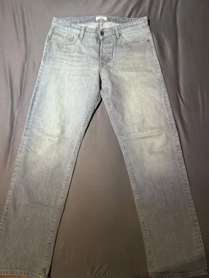 Ljusblå raka jeans från Jack and Jones  - Ljusblå jeans från Levi's med klassisk femficksdesign och raka ben. Jeansen har en enkel look med subtila slitningar och är tillverkade i mjukt denimtyg. Perfekta för en avslappnad stil och passar till det mesta.