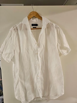 Vit linneskjorta från Riley - Klassisk vit skjorta från Riley i svalt linne. Skjortan har korta ärmar, knappar framtill och en avslappnad passform. Perfekt för varma dagar och enkel att styla till olika looks.