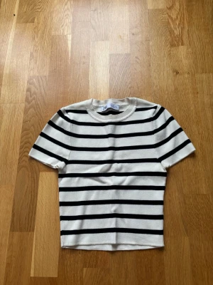 Randig kortärmad topp från Zara - Snygg kortärmad topp från Zara i vitt med svarta horisontella ränder. Modellen är kort och har rund halsringning. Materialet känns mjukt och stretchigt, perfekt för en trendig vardagslook. Säljer på grund av för liten i storleken!
